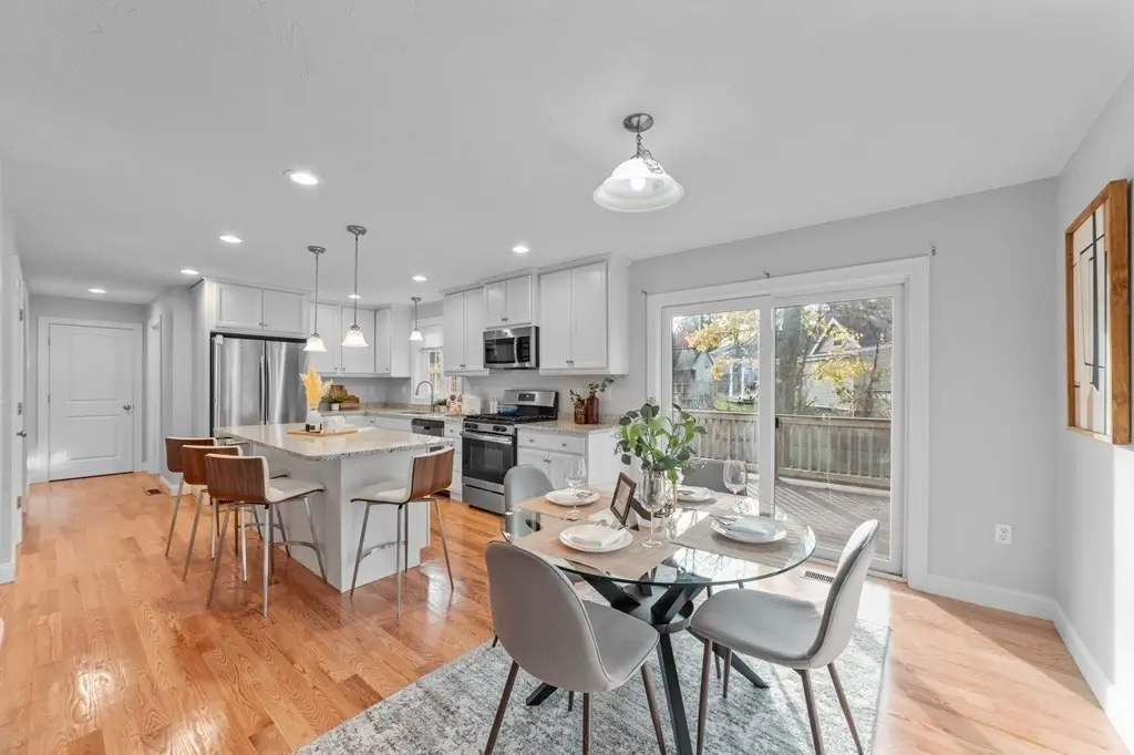 Bright kitchen and dining area with hardwood floors, island stools and a round glass table