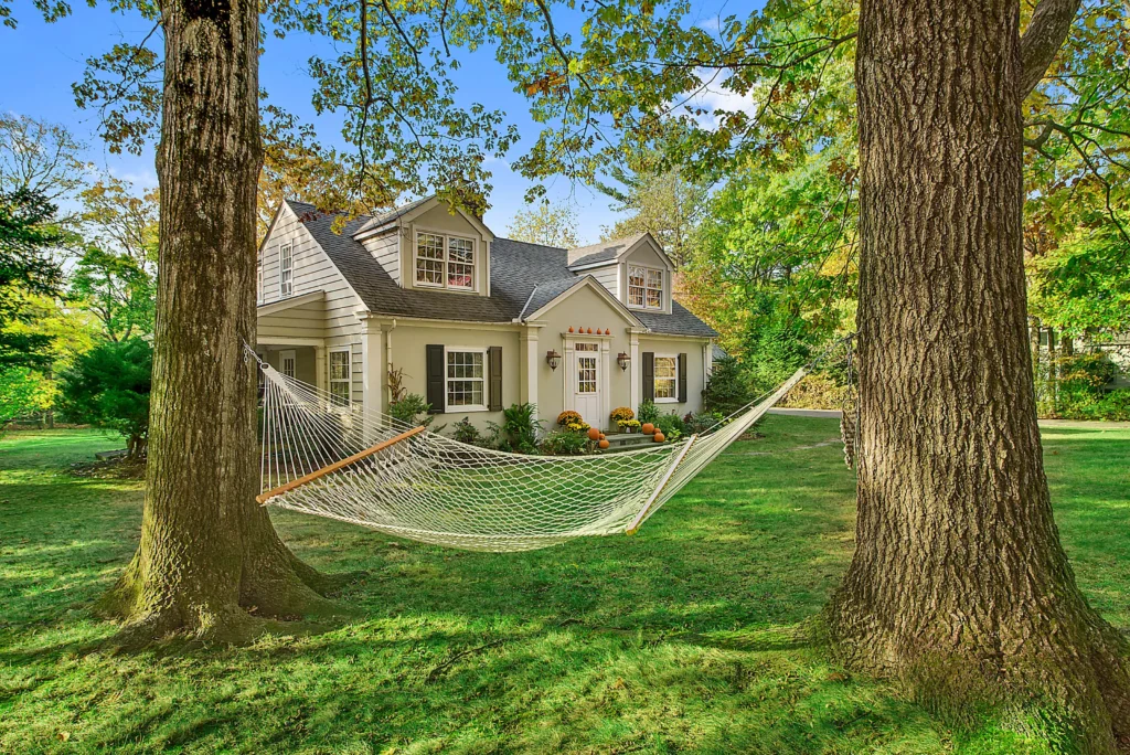 Cape Cod style house with dormers, pumpkins on the steps and a hammock between two trees in early fall