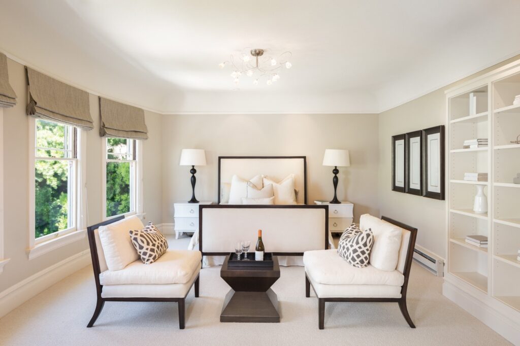 Staged bedroom with two white armchairs, a low dark table and built-in shelves by the windows