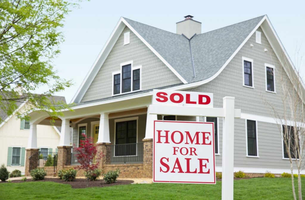 Home for sale with a sold sign on the lawn in front of a gray two-story house