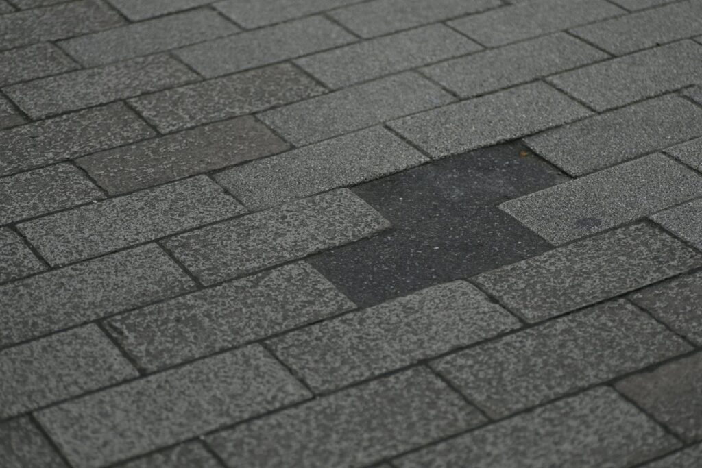 Worn gray asphalt shingle roof with one missing tab exposing the darker layer underneath